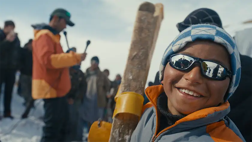 A child smiles with sunglasses in snowy mountain waither in the film Champions of the Golden Valley, from director Ben Sturgulewski whom we interview in this article