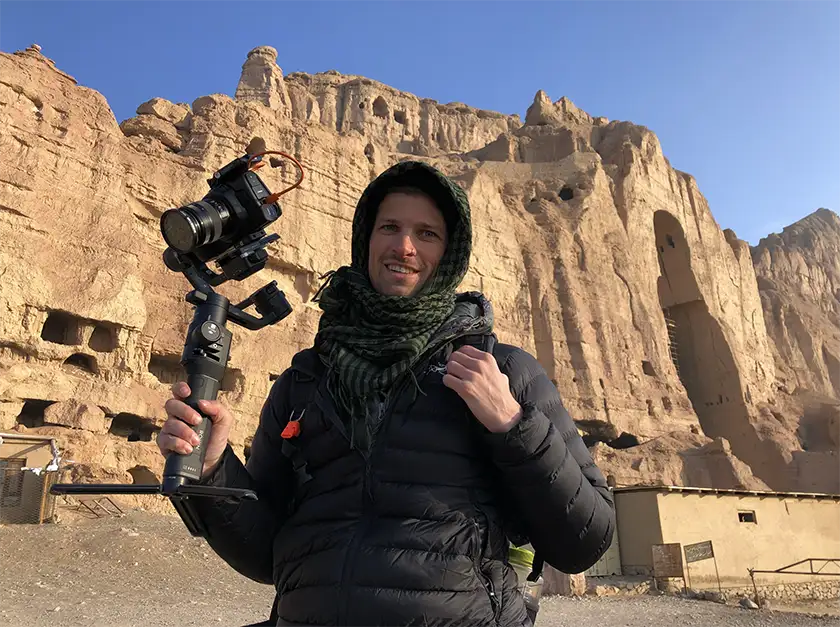 Ben Sturgulewski by the caves in the Bamyan mountains holding a camera in a behind the scenes still of the film Champions of the Golden Valley