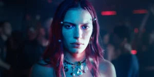 A red haired girl looks intensely at the camera in an indoor shot at night in a still from the film Come Closer