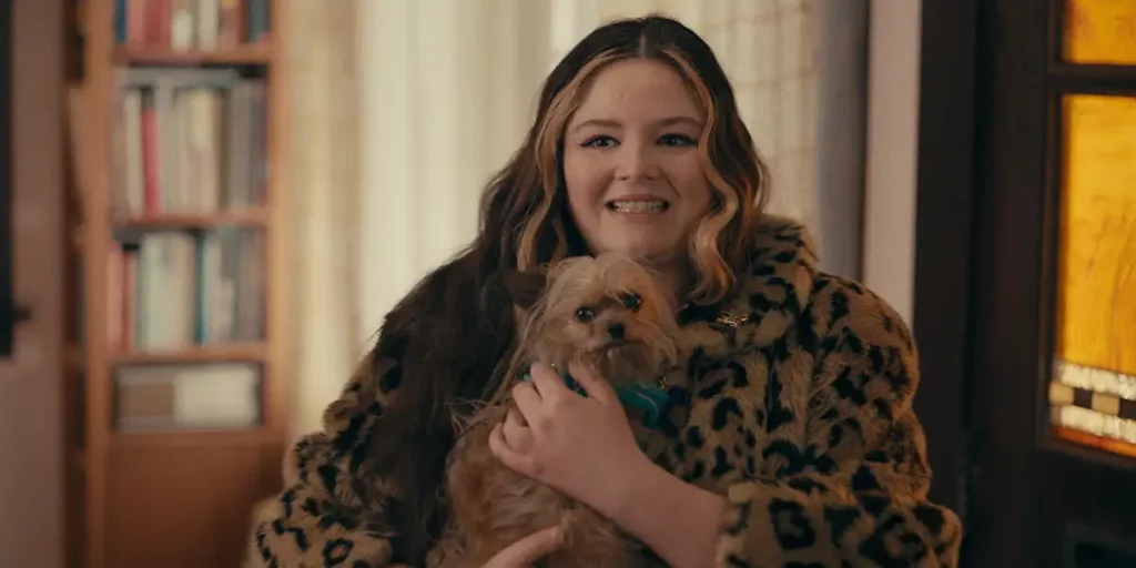 A girl with a leopard top hugs a small dog smiling in the film Cora Bora