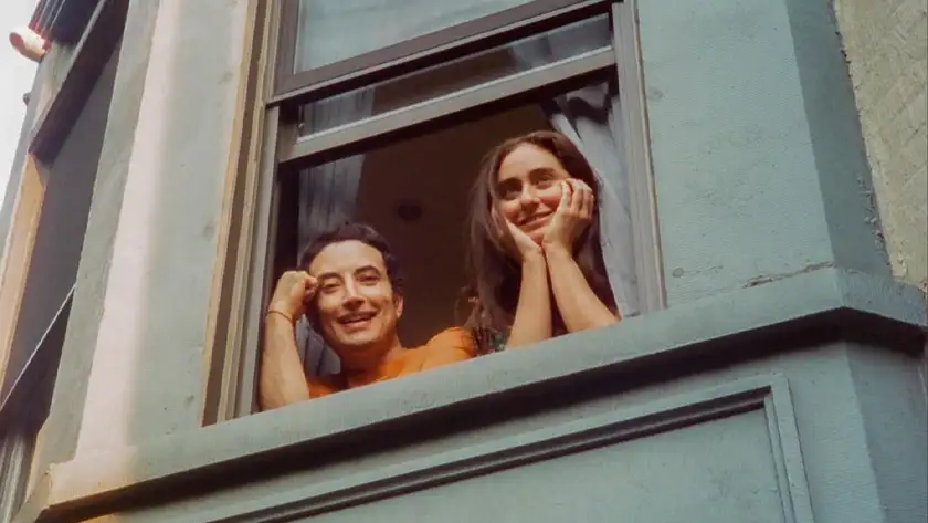 Two people look outside a blue window in a still from the 2024 film The French Italian