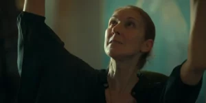 Céline Dion has her hands up in the air wearing a green vest in the 2024 film I Am: Celine Dion