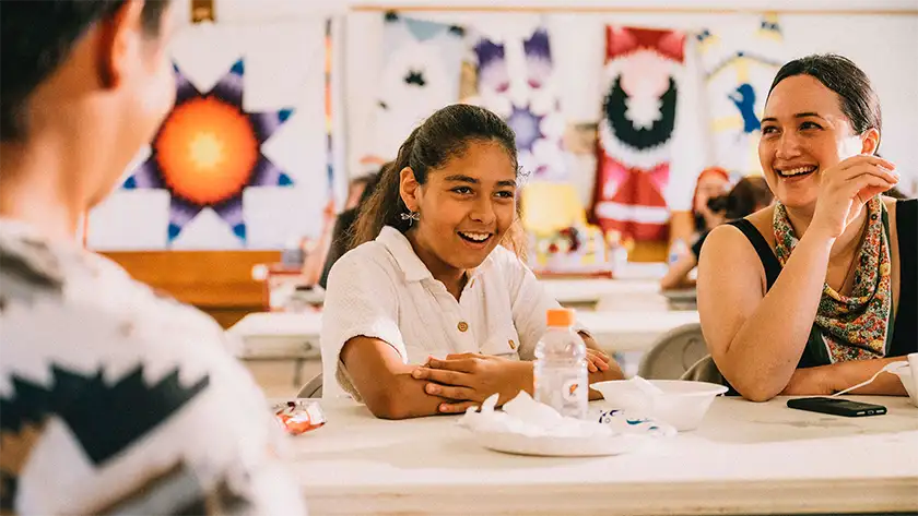 A girl and a woman laugh sitting at a table in the film Jazzy