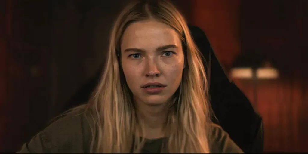 A girl with blond hair looks at the camera intensely in a still from the film Latency