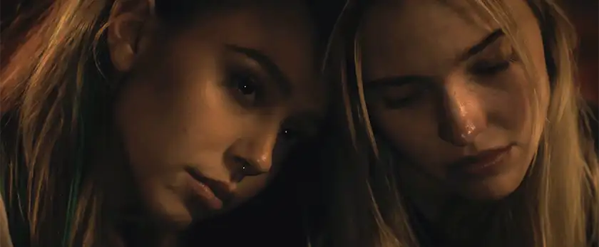 The faces of two blonde girls leaning on each other looking sad in a still from the film Latency