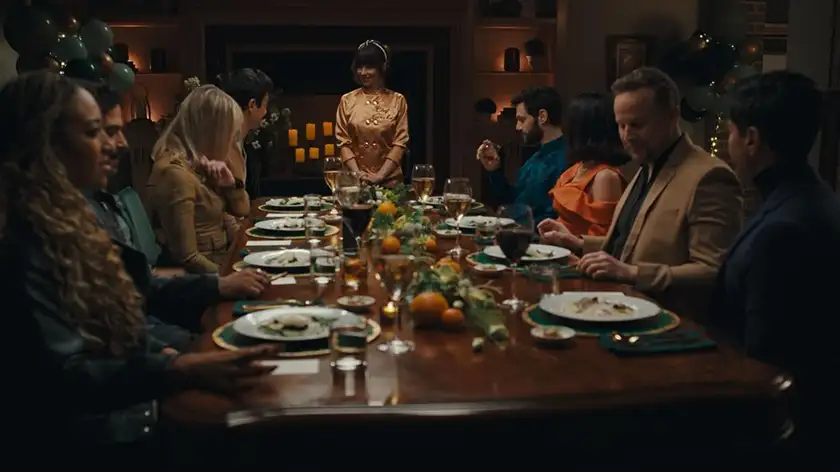 eight people sit around a dinner table with their plates full and a woman stands looking at them in the film Nuked