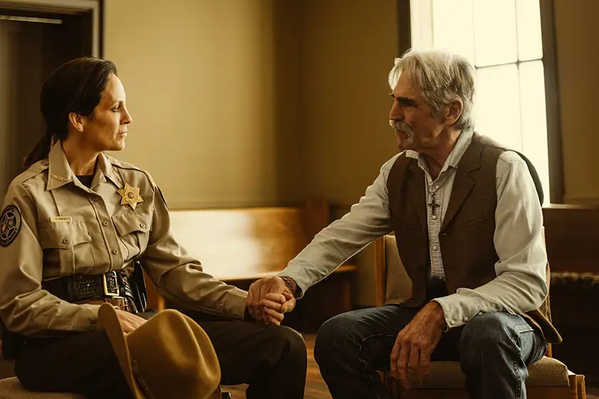 A sheriff and a man hold hands sitting in a waiting room in a still from the film Ride
