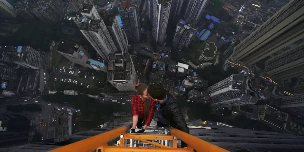 A couple kisses while holding on to a very high construction tower in China A woman does acrobatics on a dangerously high building in China in the film Skywalkers: A Love Story