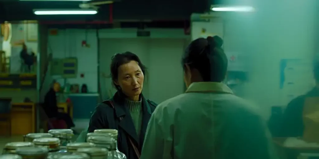 A woman talks to someone with some bottles on the table next to them in the film Some Rain Must Fall