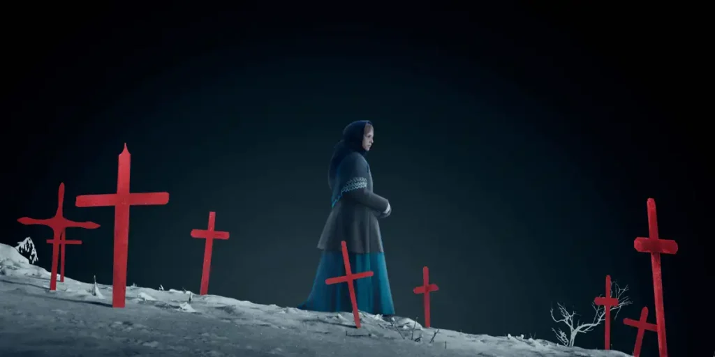 A girl walks in a cemetery between the mountains with red crosses around her in a still from Thordur Palsson's The Damned