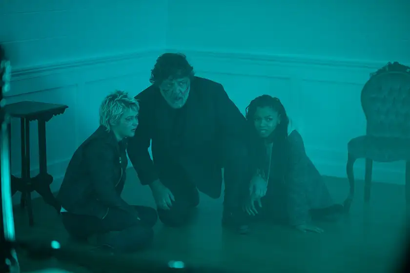 Three people crouch on the floor in the corner of a house in a photo from the 2024 film The Exorcism