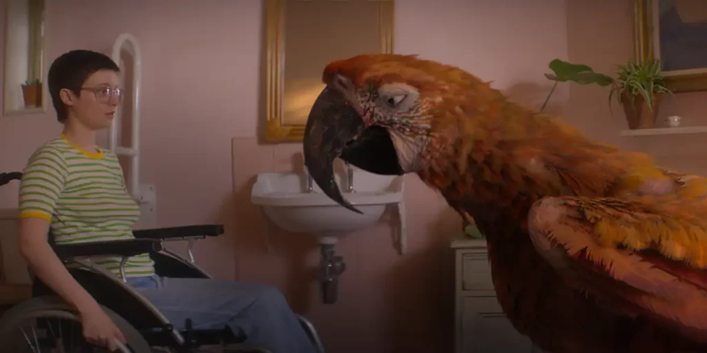 A young girl in a wheelchair sits with a giant parrot in front of her in a still from the film Tuesday
