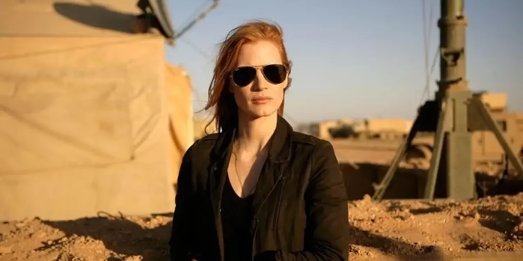 Jessica Chastain stands in the desert with black sunglasses and wearing a black shirt, with a missile behind her, in the film Zero Dark Thirty