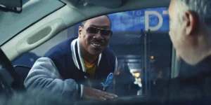 Eddie Murphy as Axel Foley leans on a car through the window, smiling, in Beverly Hills Cop: Axel F.