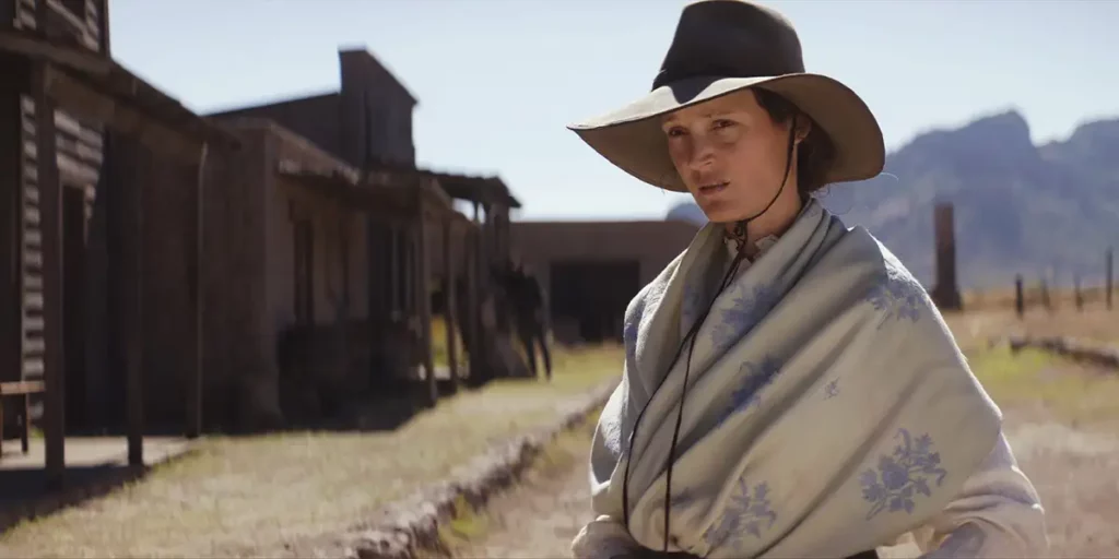 A woman stands outside of a saloon wearing a cowboy hat and a shawl in the western film The Dead Don't Hurt