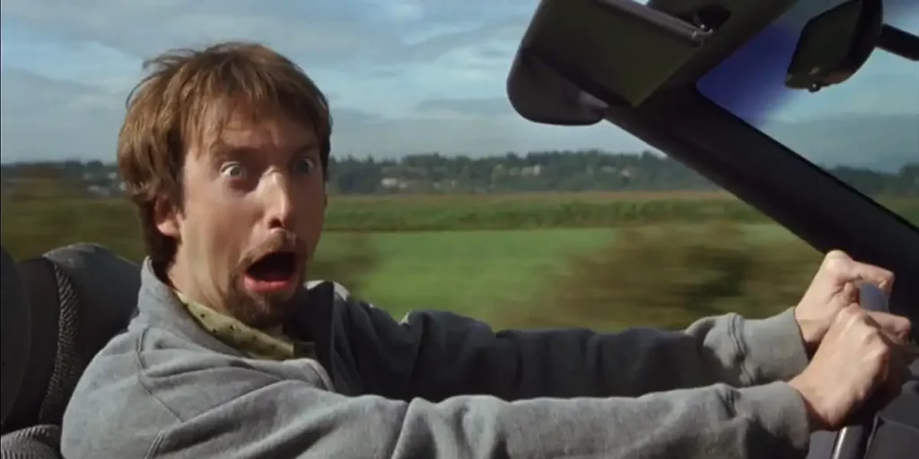 A young man drives a car while making a funny face at the camera in a still from the movie Freddy Got Fingered