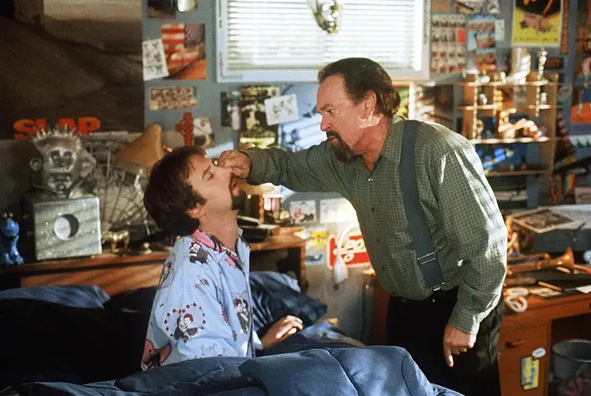 A man touches another man's face in a still from the movie Freddy Got Fingered