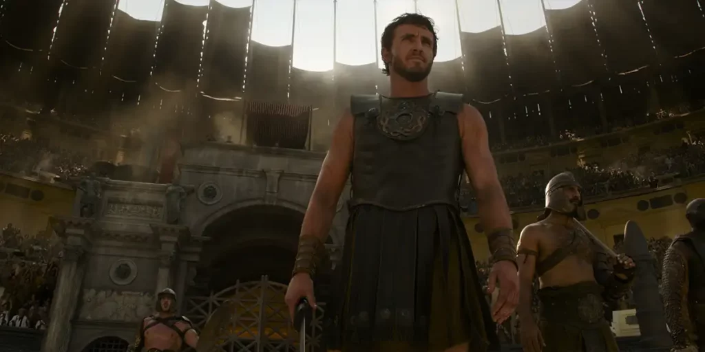 Paul Mescal stands in an arena dressed as a gladiator in Gladiator 2, in a still featured in an article with everything you should know about the movie sequel