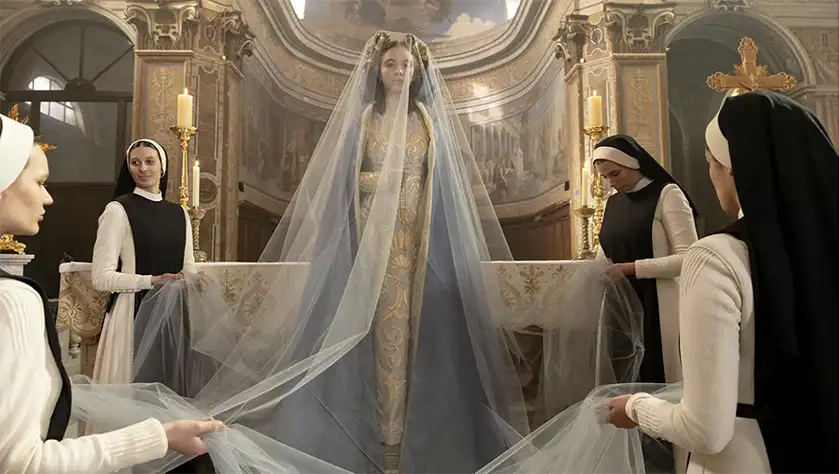 Sydney Sweeney is surrounded by nuns in a church, kneeling while holding her veil as she stands, in the film Immaculate