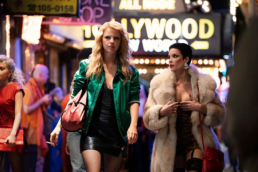 Two women walk in the street at night with a Neon Hollywood sign behind them in the film MaXXXine