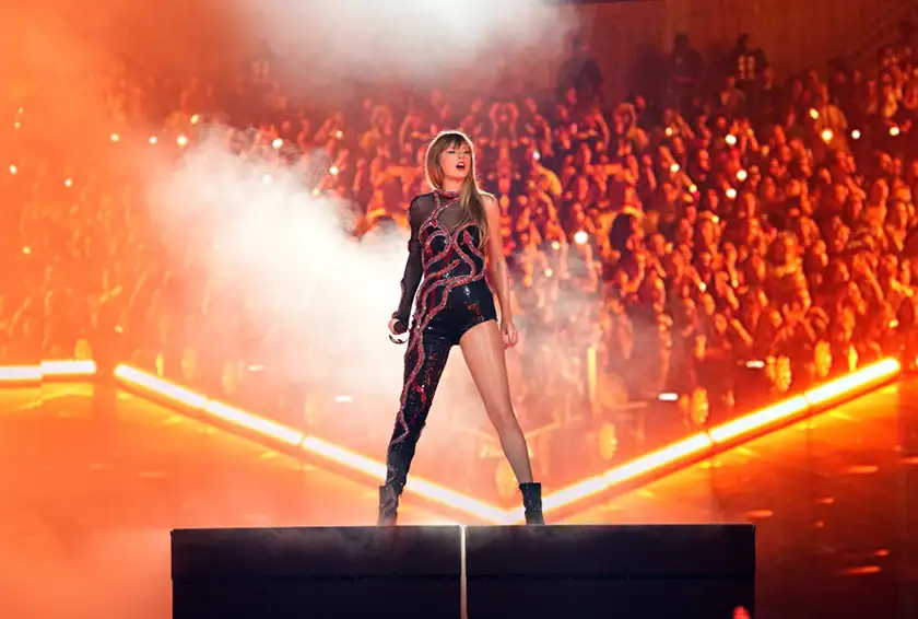 Taylor Swift is on stage wearing a black jumpsuit in The Eras Tour, in a still featured in a Loud and Clear Reviews article about how movie theaters can save themselves
