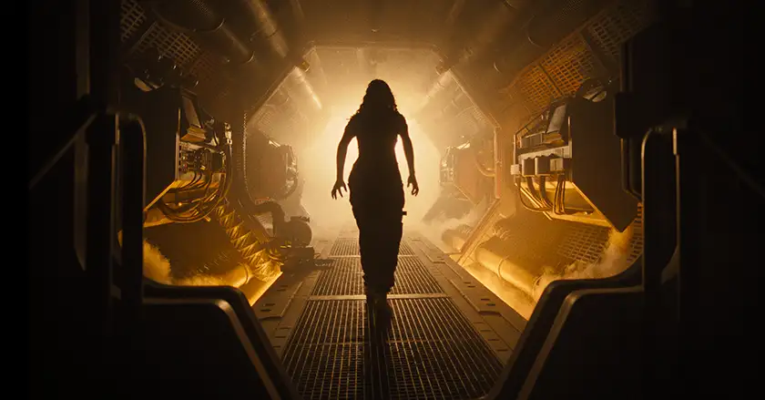 A woman walks down a spaceship's corridor toward yellow light in the 2024 film Alien: Romulus