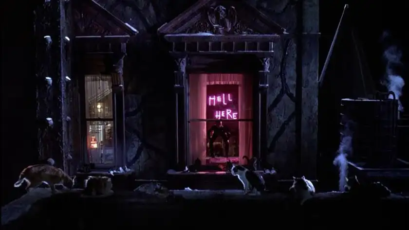 A pink neon sign, seen through a window, reads "hell here" in a shot from the movie Batman Returns