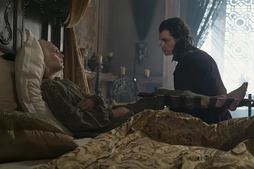 A man leans on a chair looking at another man who's in bed looking sick in Season 2 Episode 8, the season 2 finale, of House of the Dragon