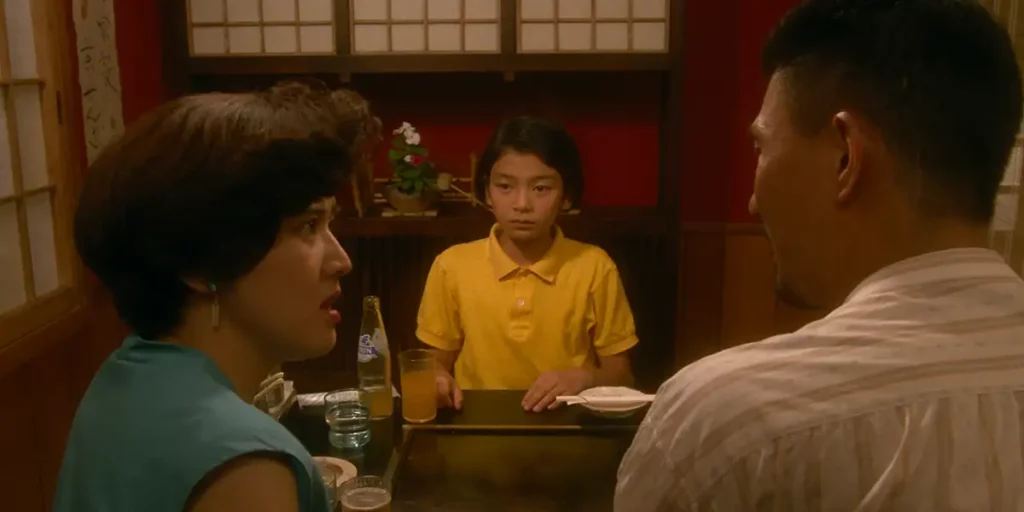 A Japanese teenage girl sits at the dinner table looking at her mother and father in front of her, in the film Moving, from Shinji Sōmai