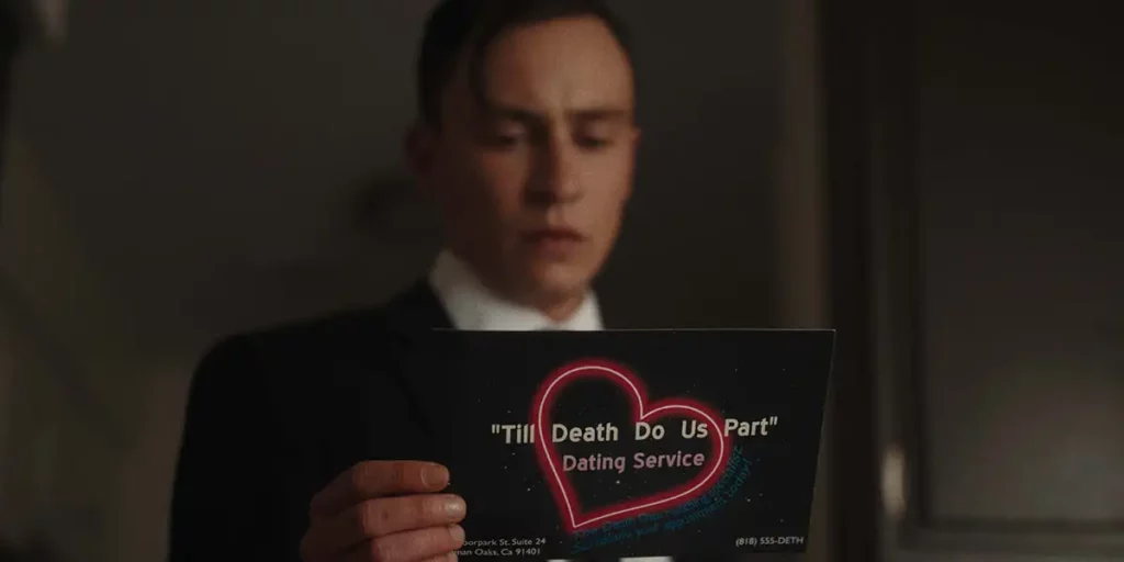 A young man holds up a card that reads "Till death do us part - dating service" on its back, reading it, in the film Running on Empty