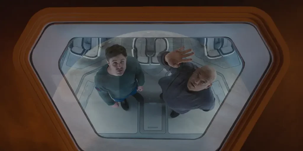 Two men on a spaceship wave to the window in a still from the film Slingshot