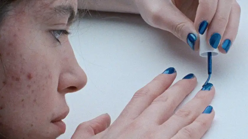 A young girl paints her nails blue in bluish