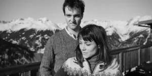 Two people smile standing close to each other with the snowy mountains behind them in a black and white still from the film The Universal Theory