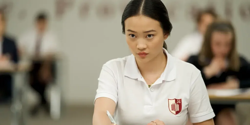 A girl wears a white t-shirt and sits in class taking an exam in a still from the film Bad Genius