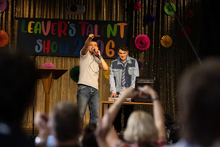 Joe Anders and Samuel Small put on a performance on a stage at the school's talent show in a still from the film Bonus Track