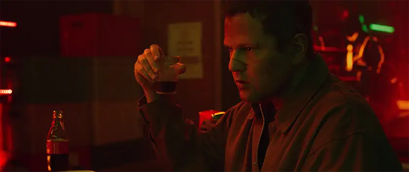 A man holds a glass with a drink in it, in a bar at night, in the film Bury Your Dead