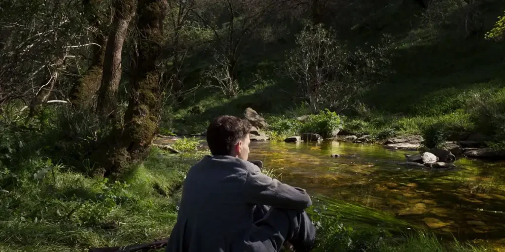 A young woman sits by the lake in the film Fire of Wind