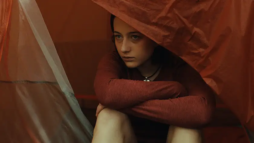 A woman looks from behind a red tent in a still from the film Good One