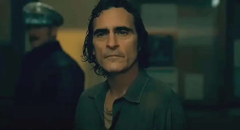 Joaquin Phoenix as Arthur Fleck wears a shirt and looks sad in the movie Joker Folie à Deux, whose ending and meaning are explained in this Loud and Clear article