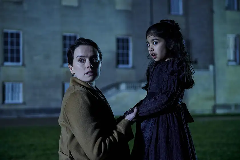 Daisy Ridley and a child stand outside a house at night in a still from the film Magpie