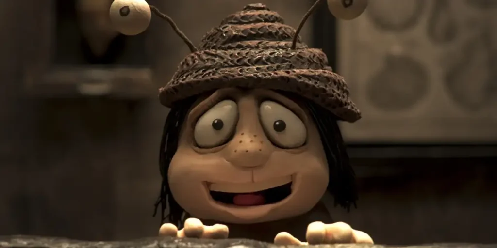 A stop motion character with big eyes and a funny hat smiles looking at us in a still from the film Memoir of a Snail