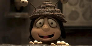 A stop motion character with big eyes and a funny hat smiles looking at us in a still from the film Memoir of a Snail