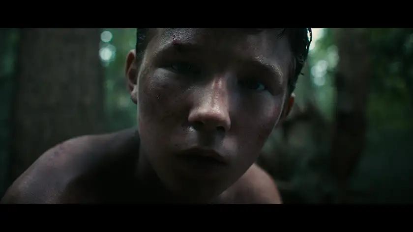 A child looks into the camera in the woods in a still from the film Lost on a Mountain in Maine