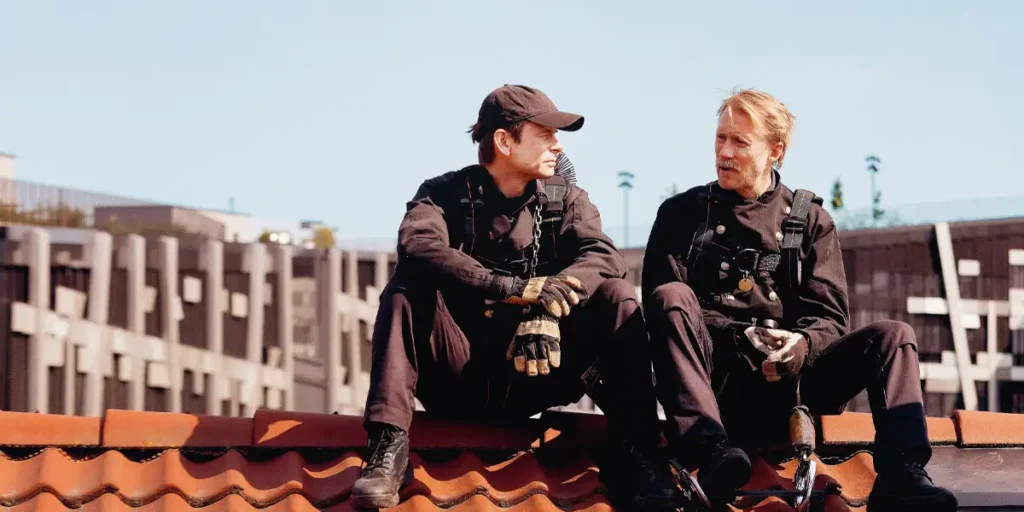 Thorbjørn Harr and Jan Gunnar Røise sit on a roof as "Supervisor" and "Chimney Sweeper" in Dag Johan Haugerud's film "Sex"