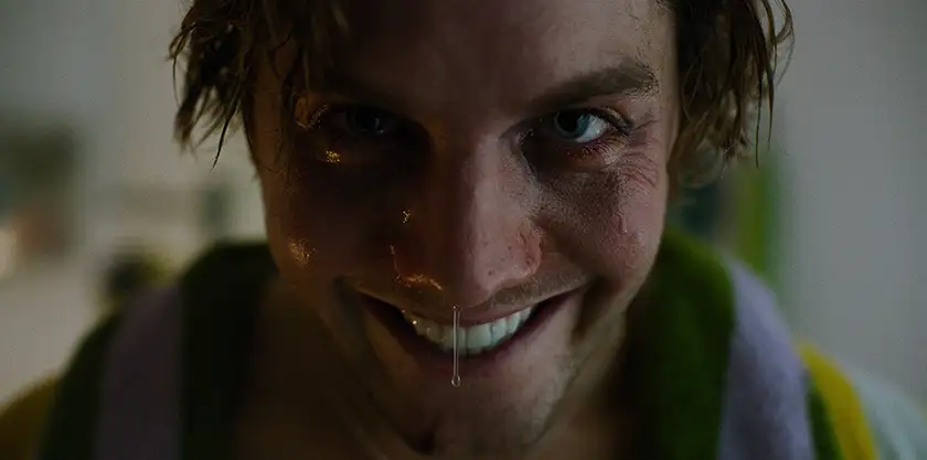 A man smiles creepily with snot coming out of his nose in a still from the movie Smile 2