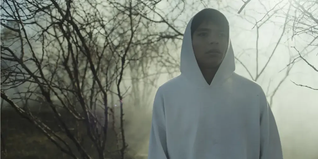 A man wears a white hoodie in a still from the film Sujo