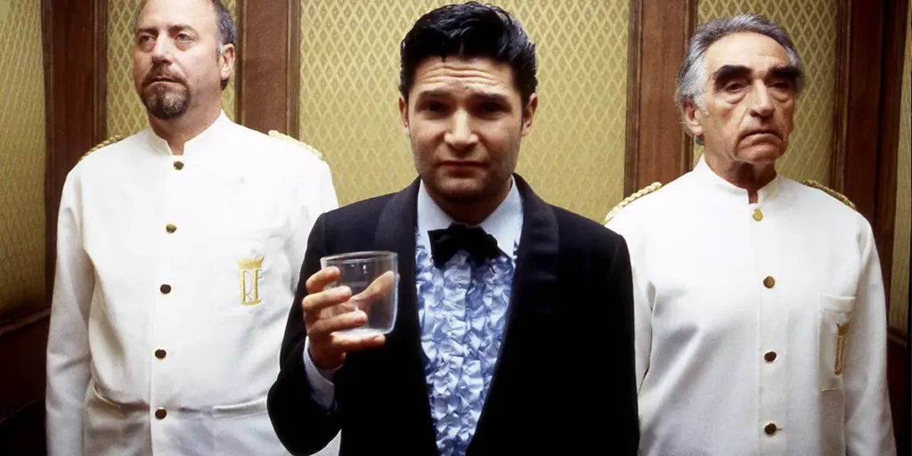 A man holds up a glass with two chefs on either side in an elevator in a scene from the film The Birthday