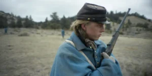 A woman soldier holds a rifle and looks to her left in a still from the Roberto Minervini film The Damned