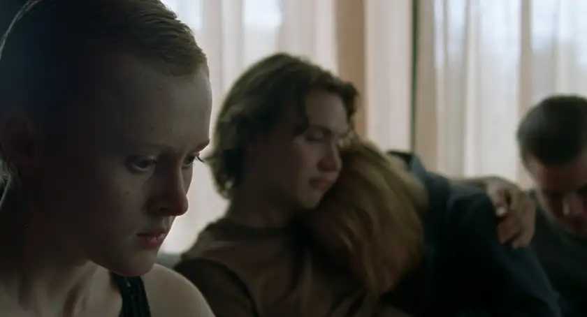 Elín Hall looks sad, on her own while some other characters hug in the background, in When the Light Breaks, whose director, Rúnar Rúnarsson, we also interview