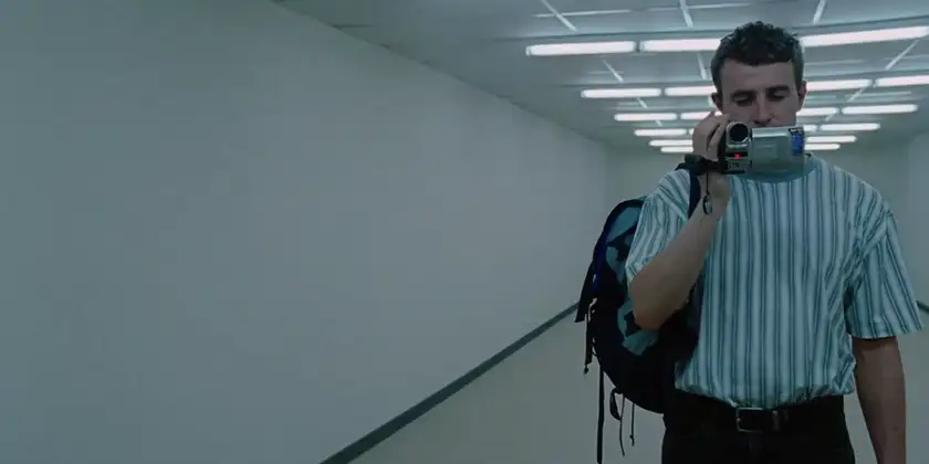 Calum walks in an empty corridor holding a camera in a scene from Charlotte Wells's Aftersun, which is explained in this article where we decode Sophie's memories